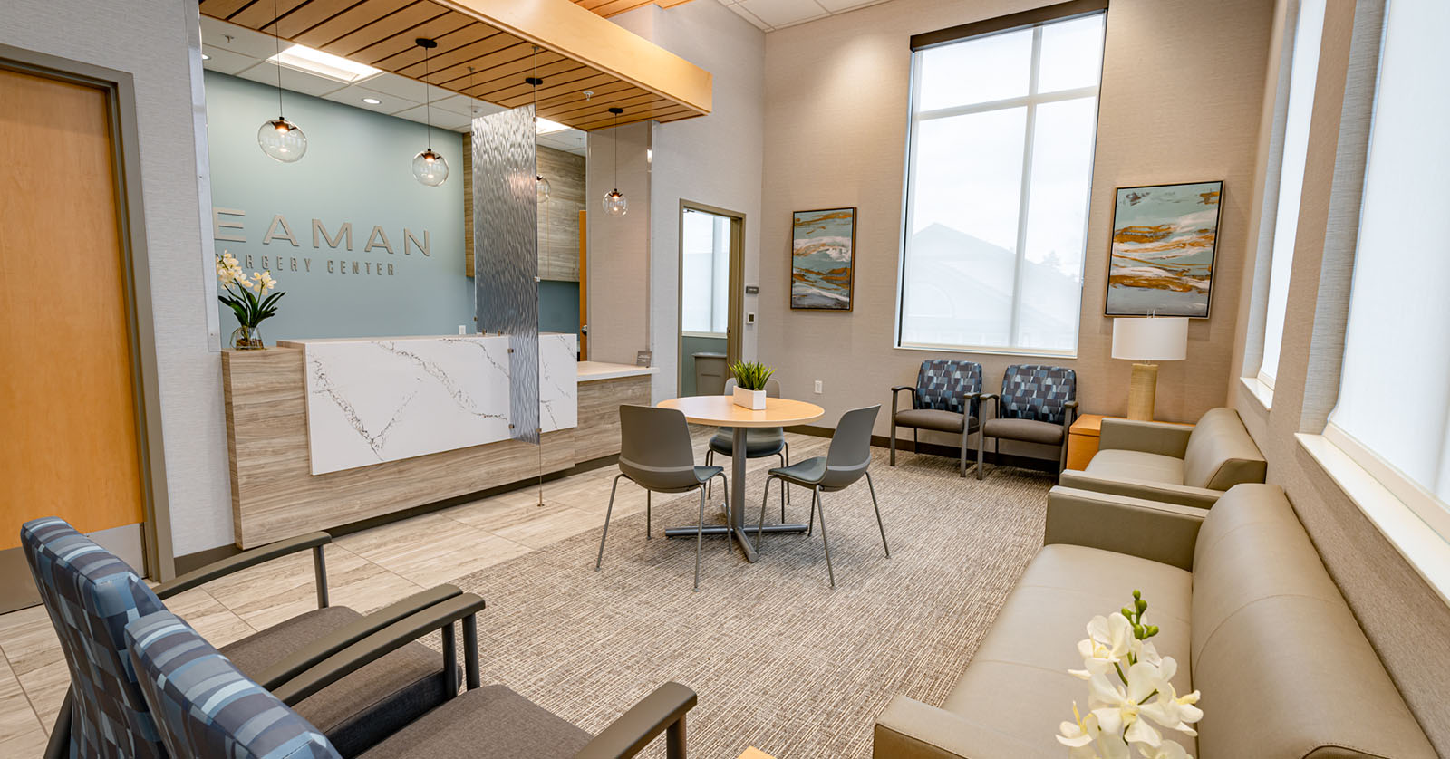 Contemporary clinic waiting area with a marble reveal reception desk blue accent wall and round table with four chairs under pendant lights   esprit® cosmetic surgeons